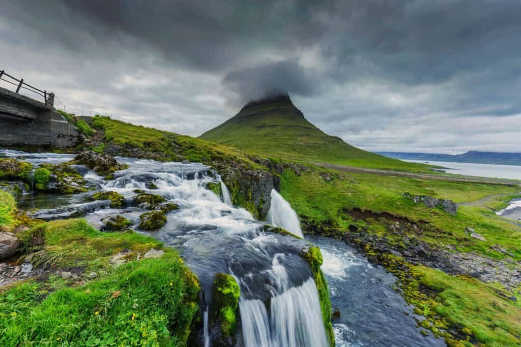 Moody clouds over Kirkjufell mountain and waterfall flowing in summer at Iceland 